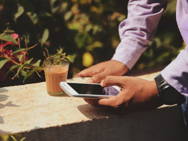 飲み物を用意して外でスマホを見ている男性